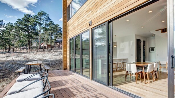 Ein modernes Haus mit einer Holzdiele, einem Essbereich mit Tisch und Stühlen sowie großen Glasfenstern, die zu einem Innenraum führen.