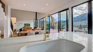 Eine moderne Küche mit einer großen Spüle, ein Essbereich mit Sofa und Tisch und große Fenster mit Blick auf die Berge.