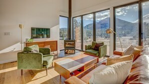 Ein modernes Wohnzimmer mit Kamin, großen Fenstern und Bergblick.