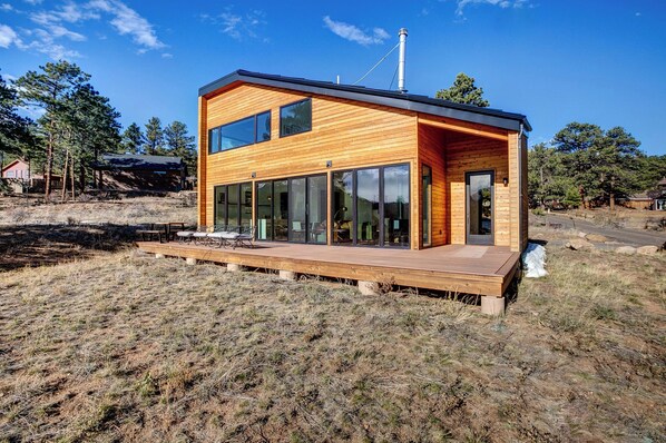 Una cabaña de madera moderna con amplios ventanales, una terraza y una chimenea.