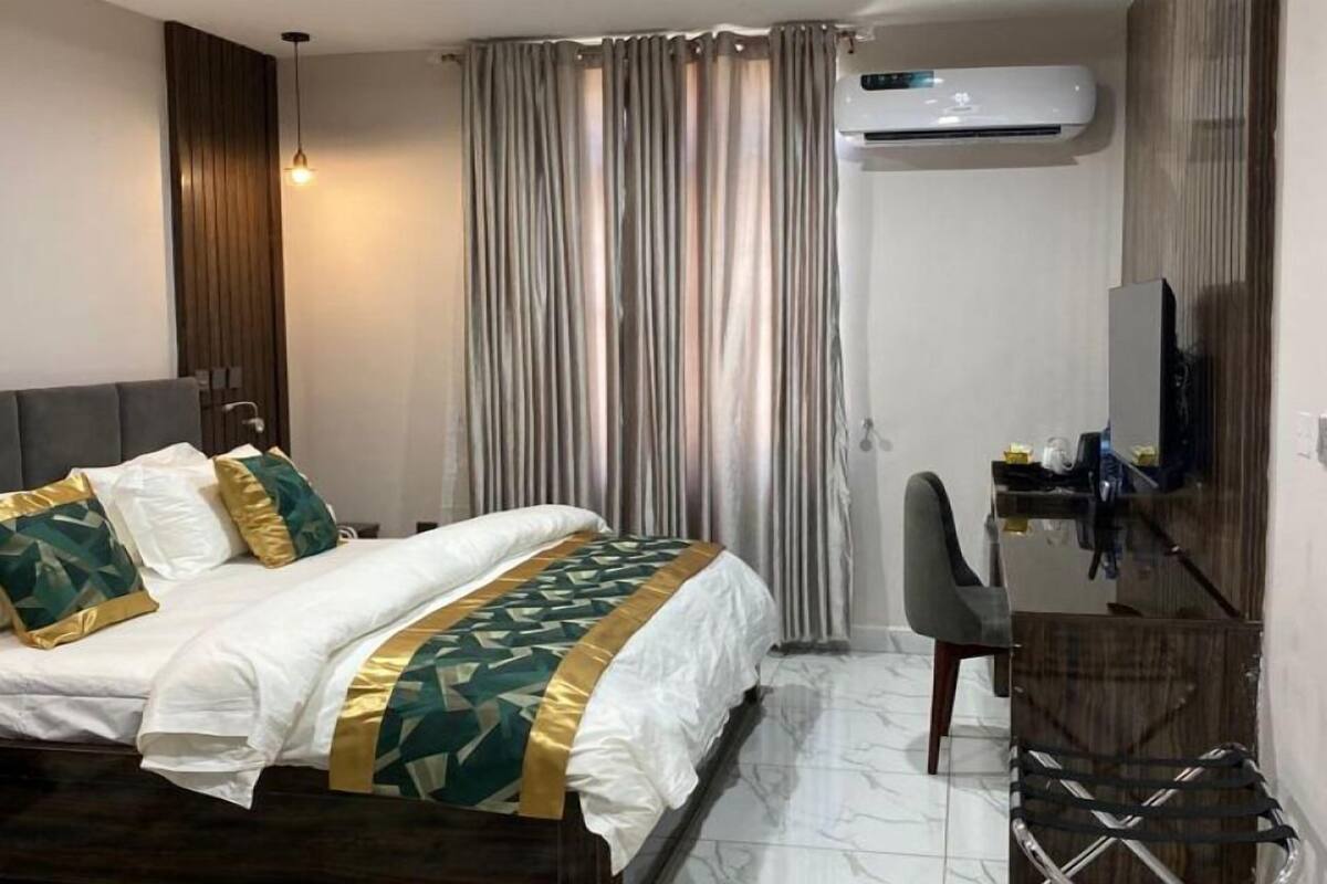 A hotel room with a bed, a desk, a chair, and an air conditioning unit.