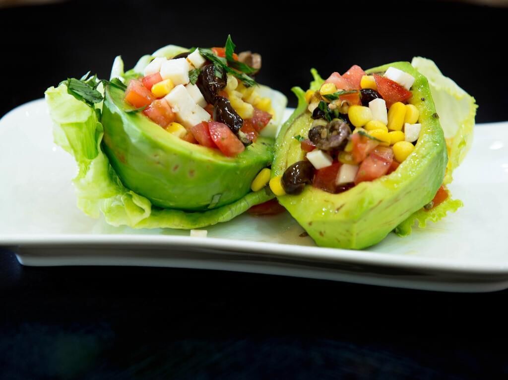 Two avocado halves filled with a salad, placed on a white plate.