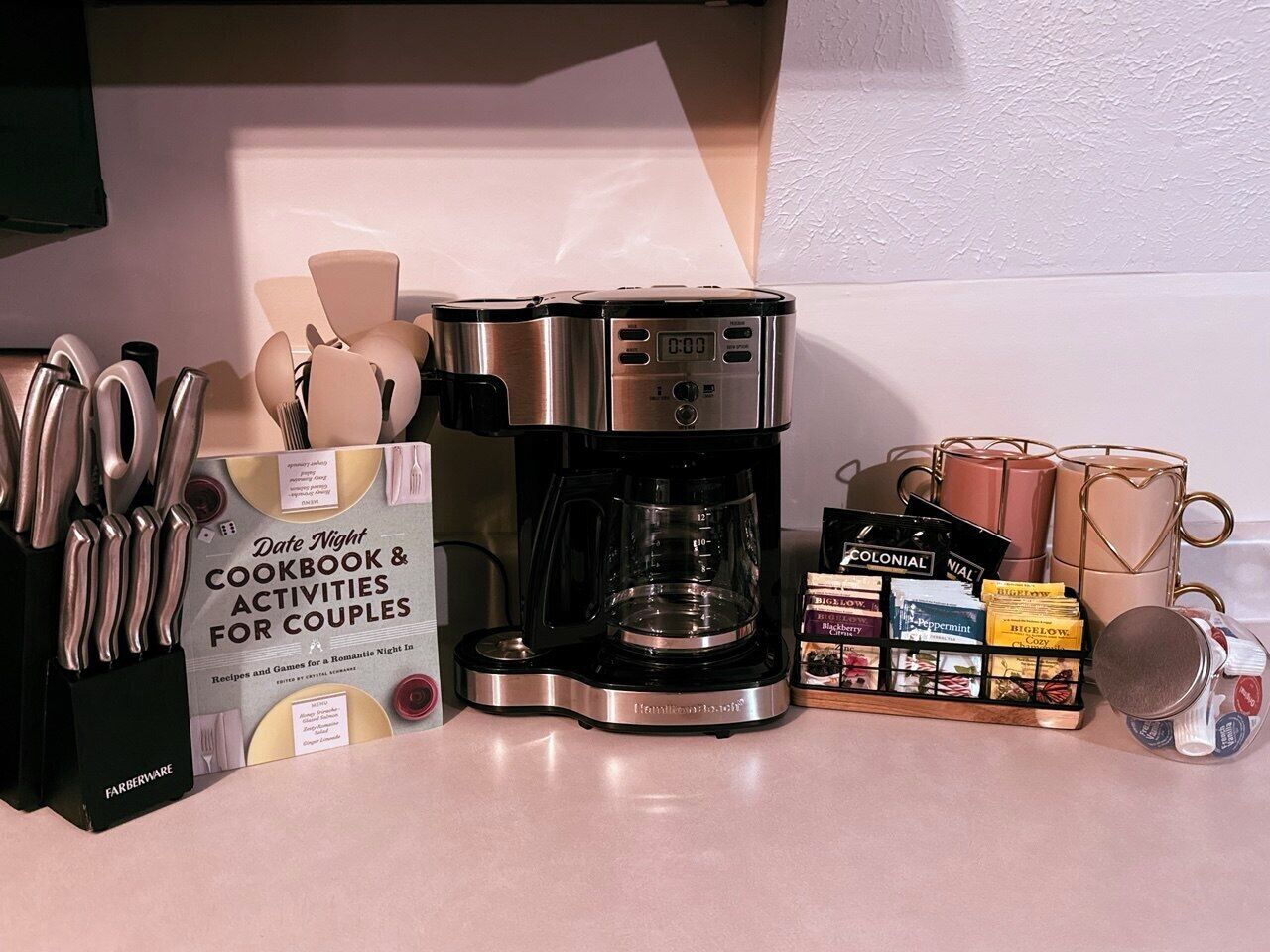 A kitchen counter with a coffee maker, a date night cookbook, a knife set, and a mug holder.
