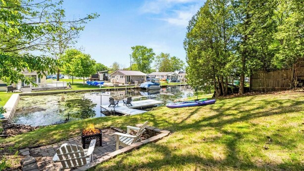 A lakeside property with a dock, boats, and a grassy area with outdoor seating.
