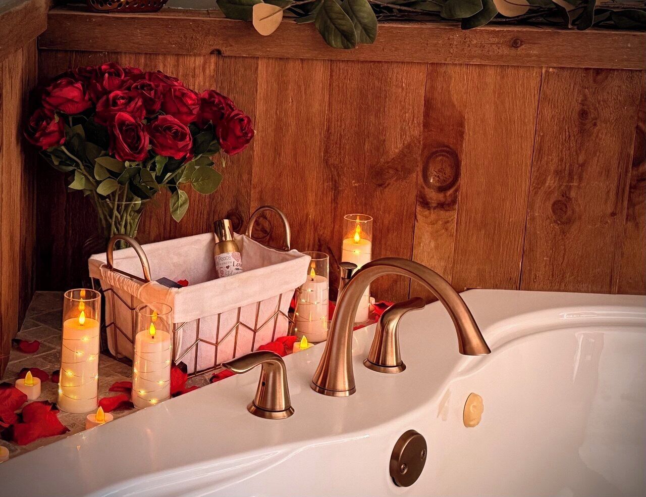 A bathroom with a white bathtub, a wooden bench, and a vase of red roses.