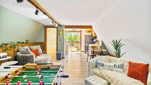 A cozy living room with a foosball table, a sofa with a 'OUR happy PLACE' pillow, and a dining area with a table and chairs.