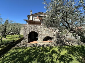 A stone building with two arched entrances, surrounded by olive trees and a well-maintained lawn.