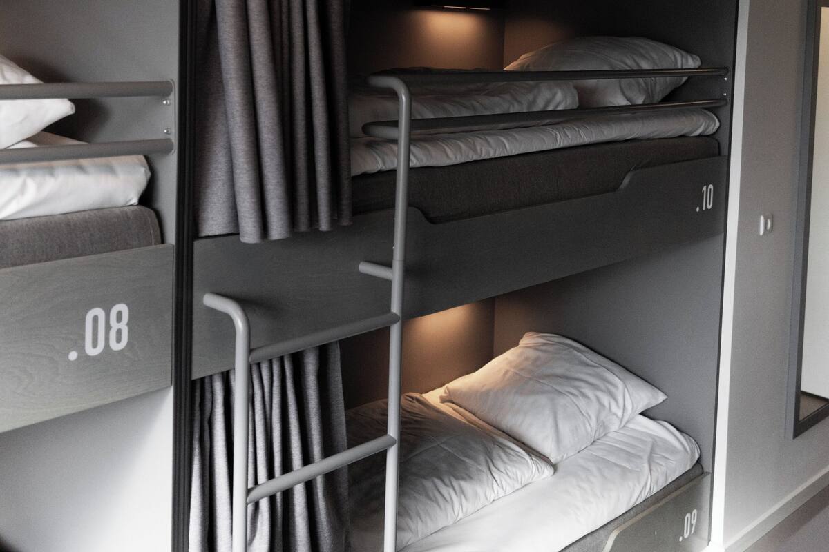 A bunk bed with three levels, each with a mattress and pillows. There is a ladder on the left side for access to the upper bunk.