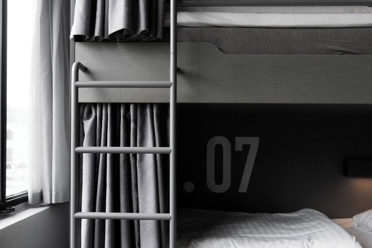 A bunk bed with a ladder, a window with curtains, and a wall with a large number.