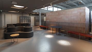 Et moderne loungeområde med en buet sofa, runde borde og bænke. Der er skabe i baggrunden og en stor væg med et geometrisk mønster.