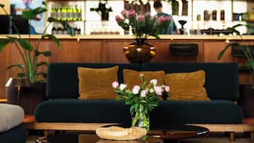 A bar area with a dark green sofa, a wooden bar counter, and a vase with flowers on a coffee table.