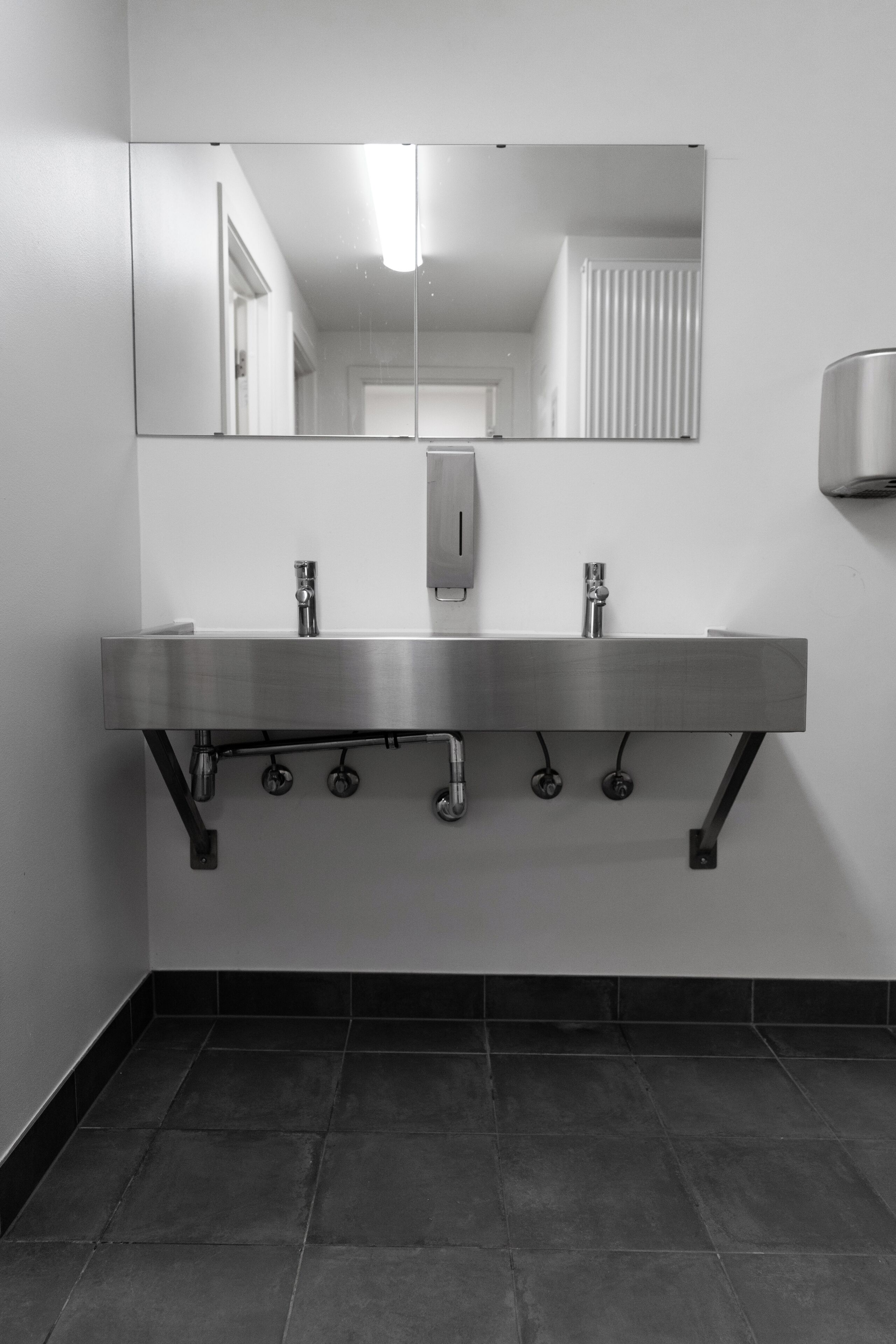 Un baño moderno con un lavamanos de acero inoxidable, un espejo y un secamanos.