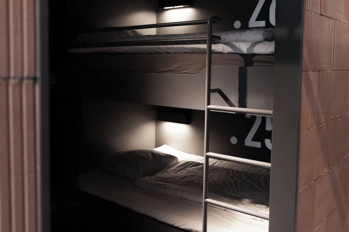 A bunk bed with a ladder, a small shelf, and a number '26' visible on the wall.