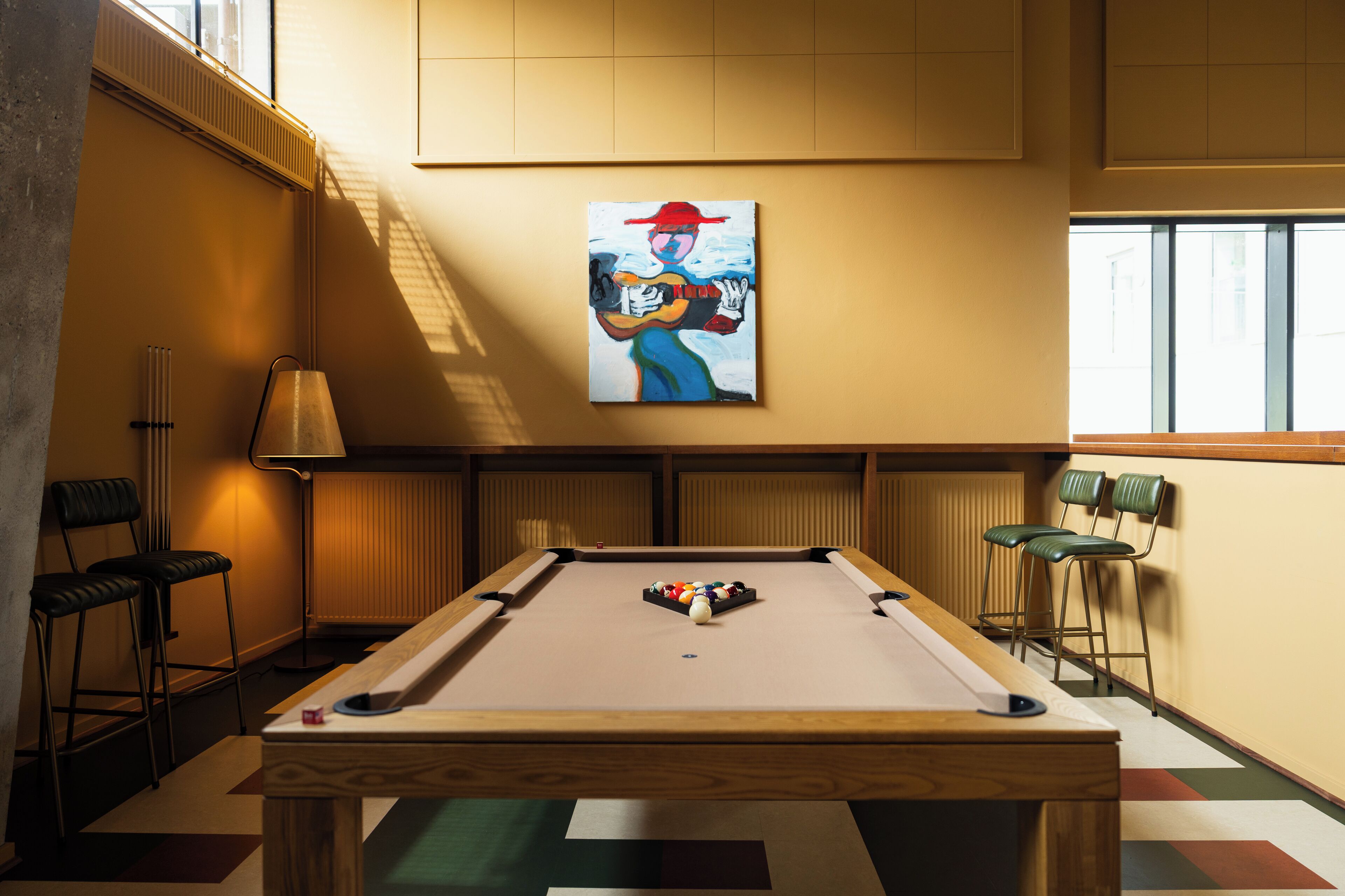 A pool table in a room with a painting above it, chairs, and a lamp.