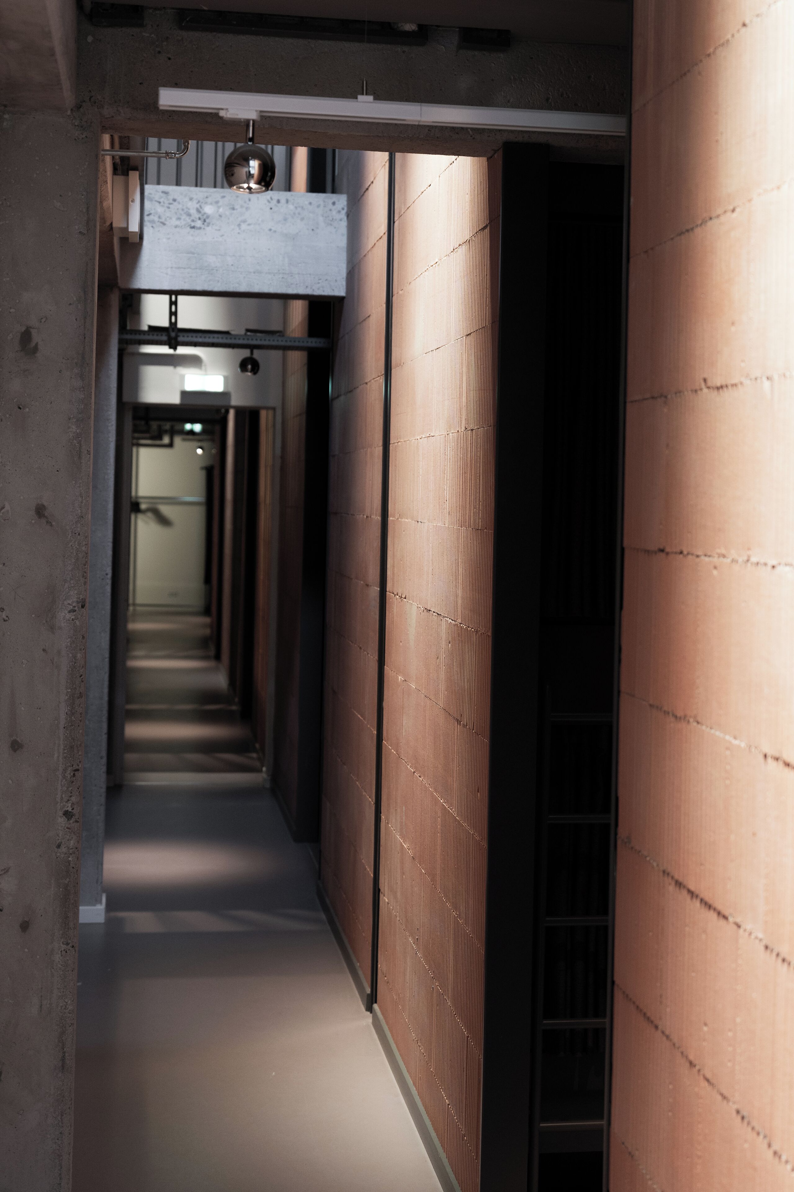 A narrow hallway with a concrete floor and walls, leading to a dark room at the end.