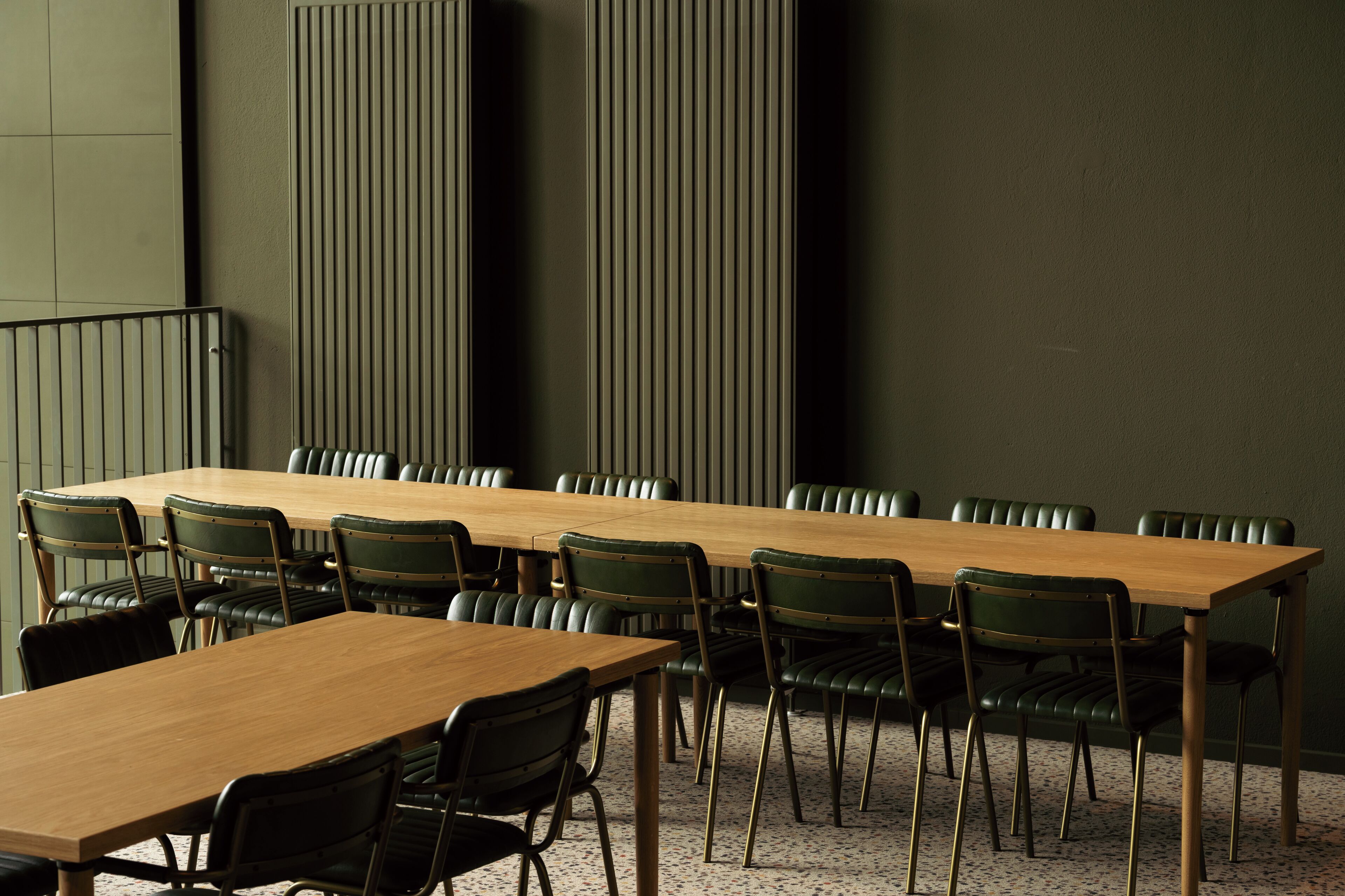 Een vergaderruimte met een lange houten tafel en groene stoelen bekleed met stof.