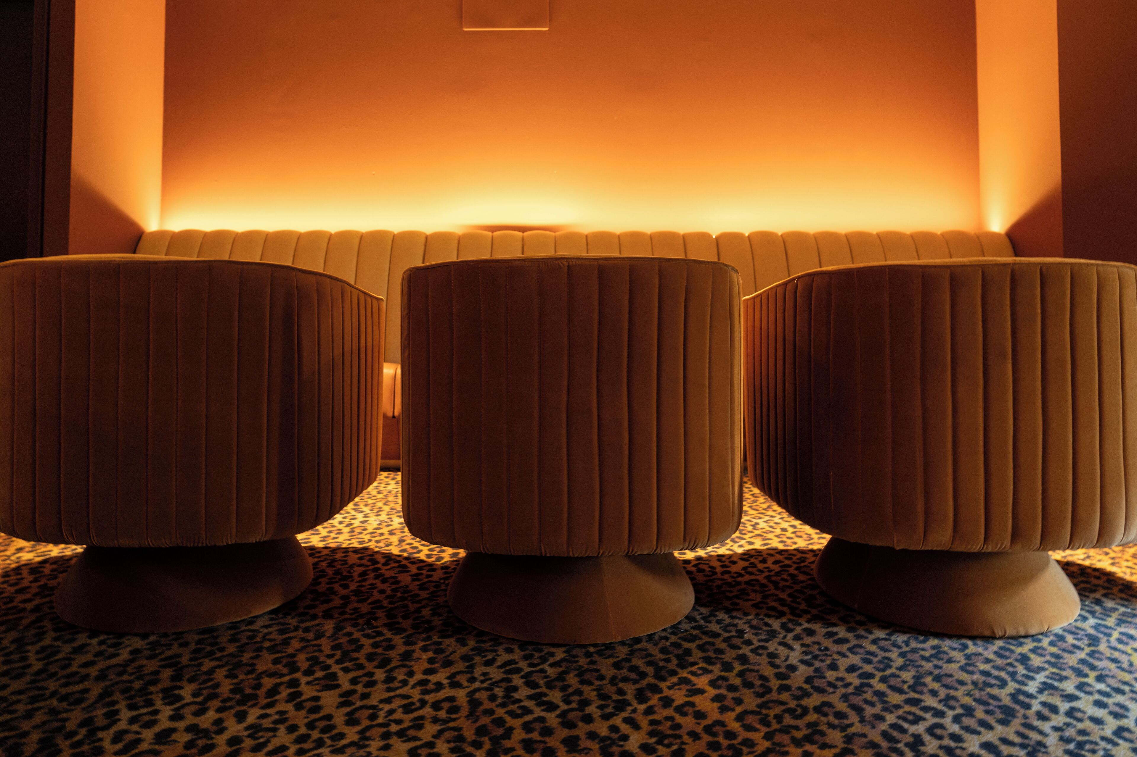 Three upholstered ottomans with a ribbed design, placed on a leopard print carpet, against a wall with a warm light source.