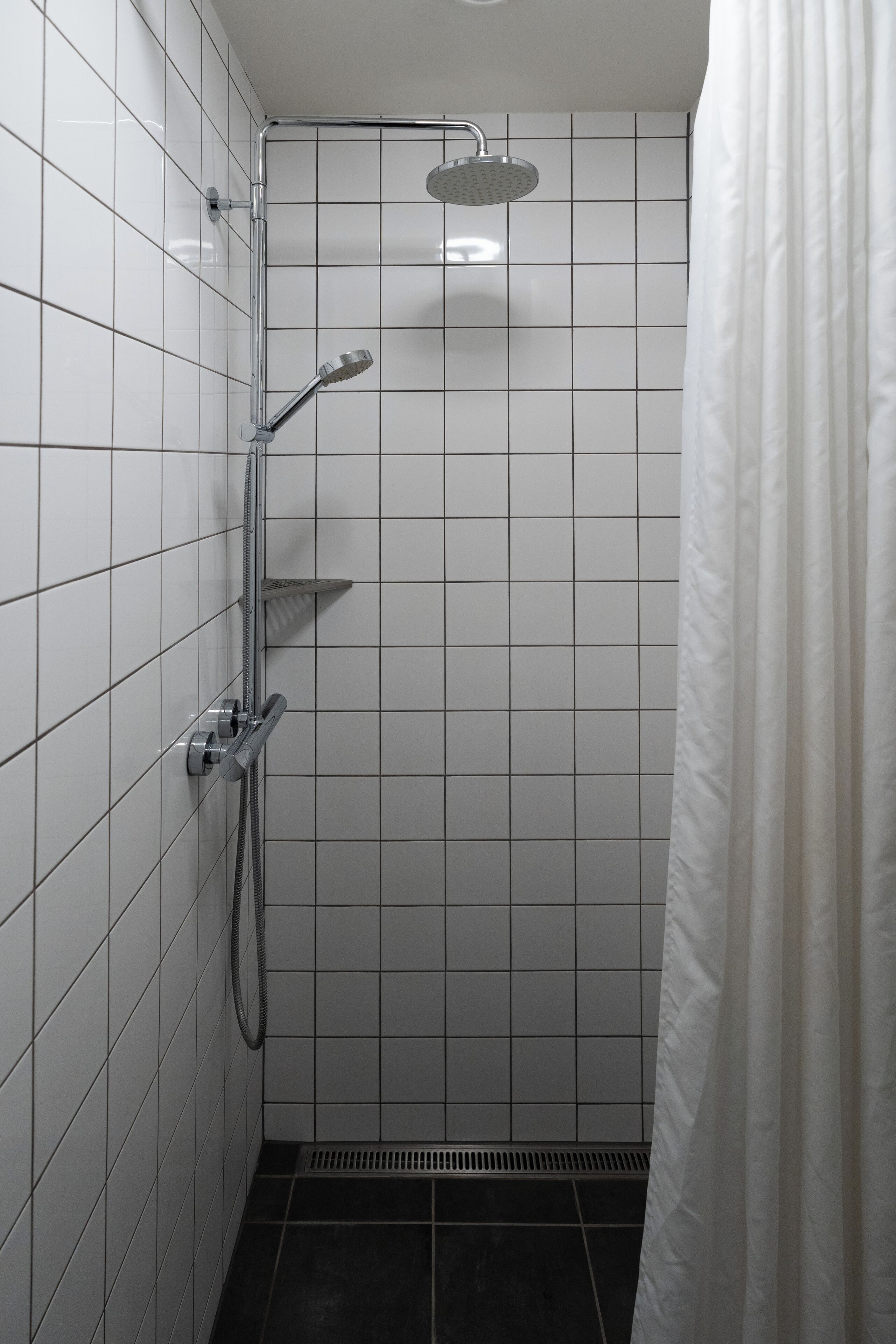 Ein kleiner Duschbereich mit Fliesen, einer Handbrause und einem am Wand montierten Wasserhahn.