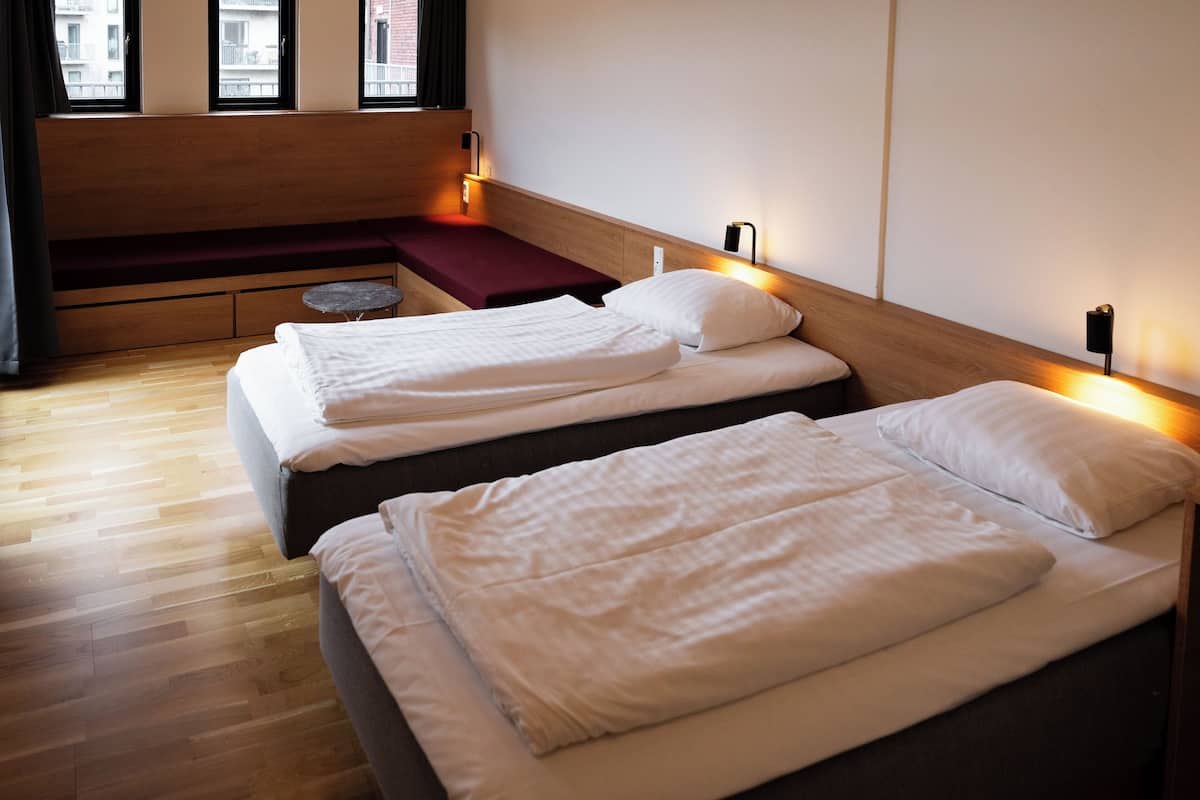 A hotel room with two beds, a wooden bench, and a small table.