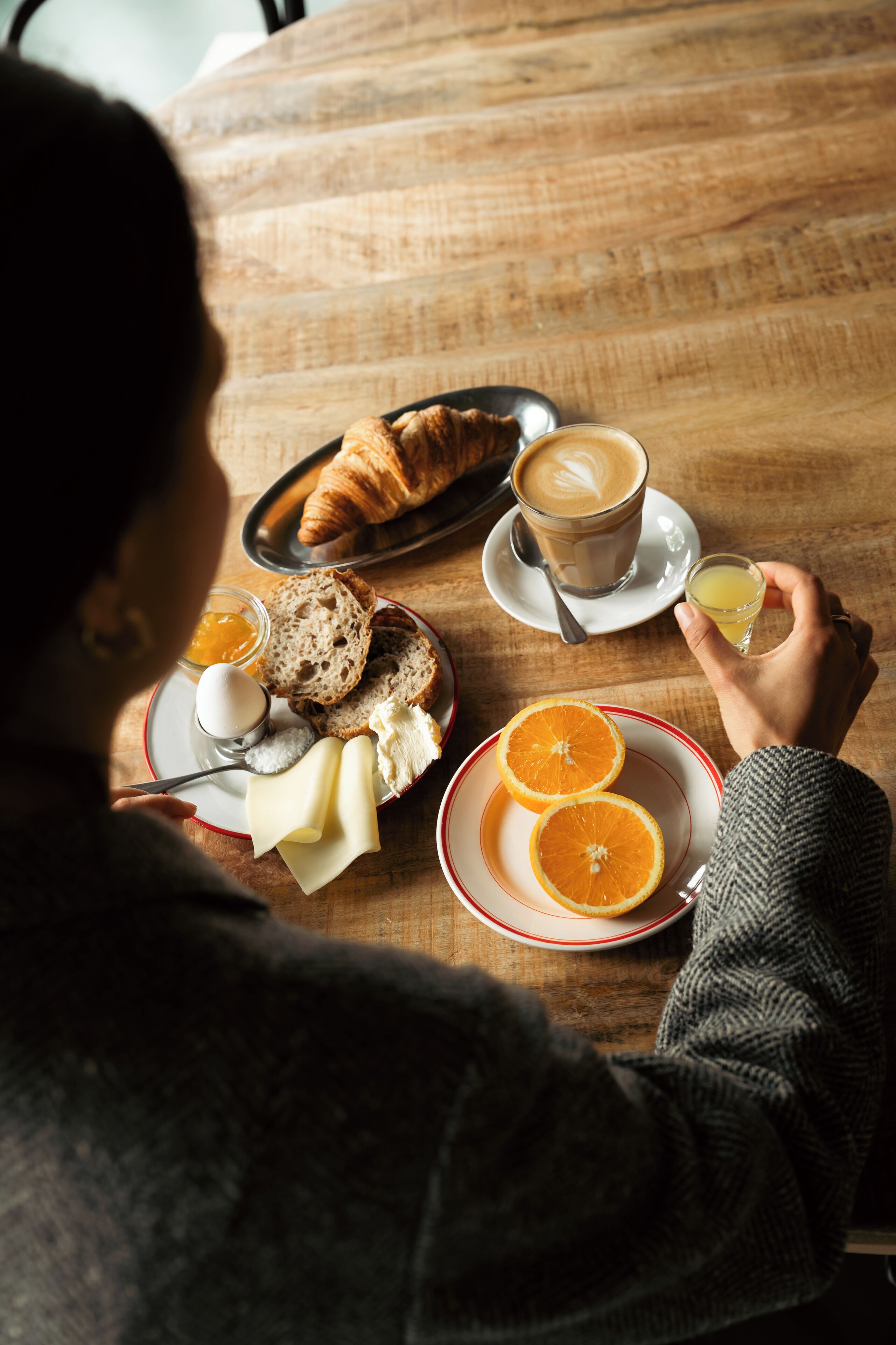 A wooden table with breakfast items including croissants, coffee, orange slices, and a glass of juice.