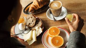 A wooden table with breakfast items including croissants, coffee, orange slices, and a glass of juice.