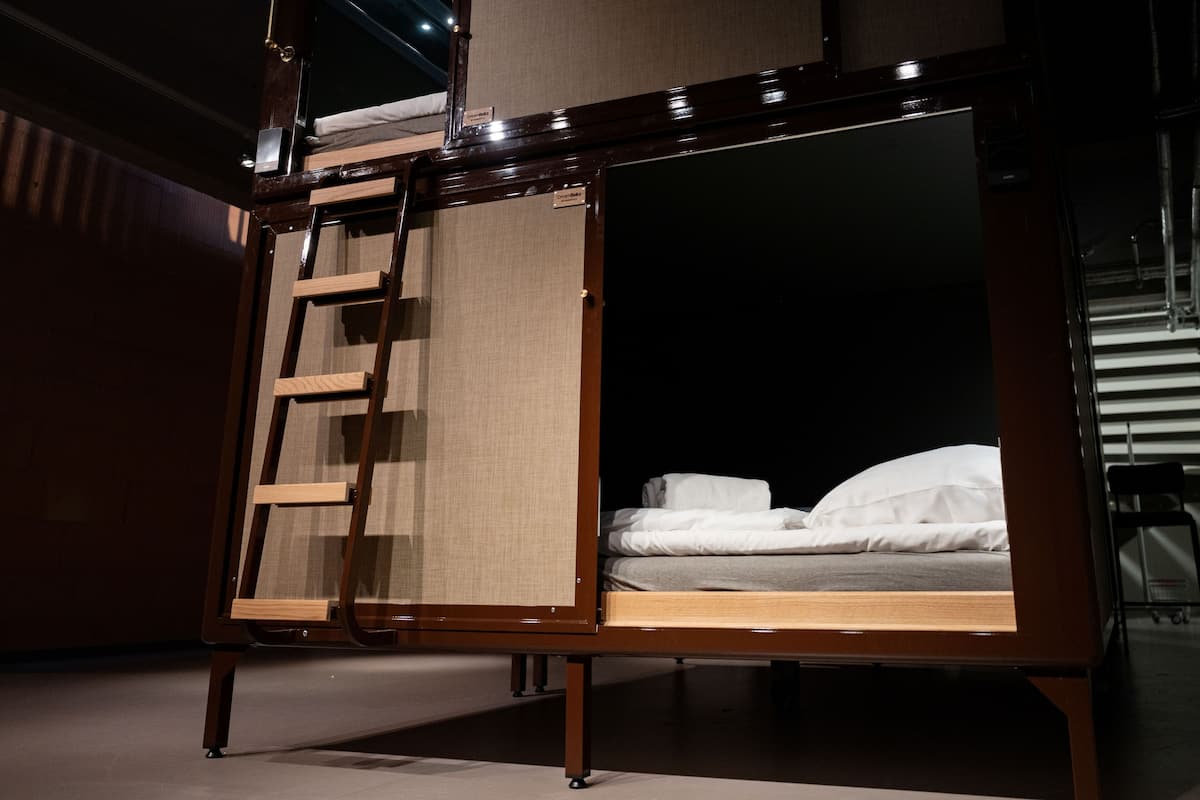 A bed with a wooden frame and a ladder, a dark interior, and a visible wall.