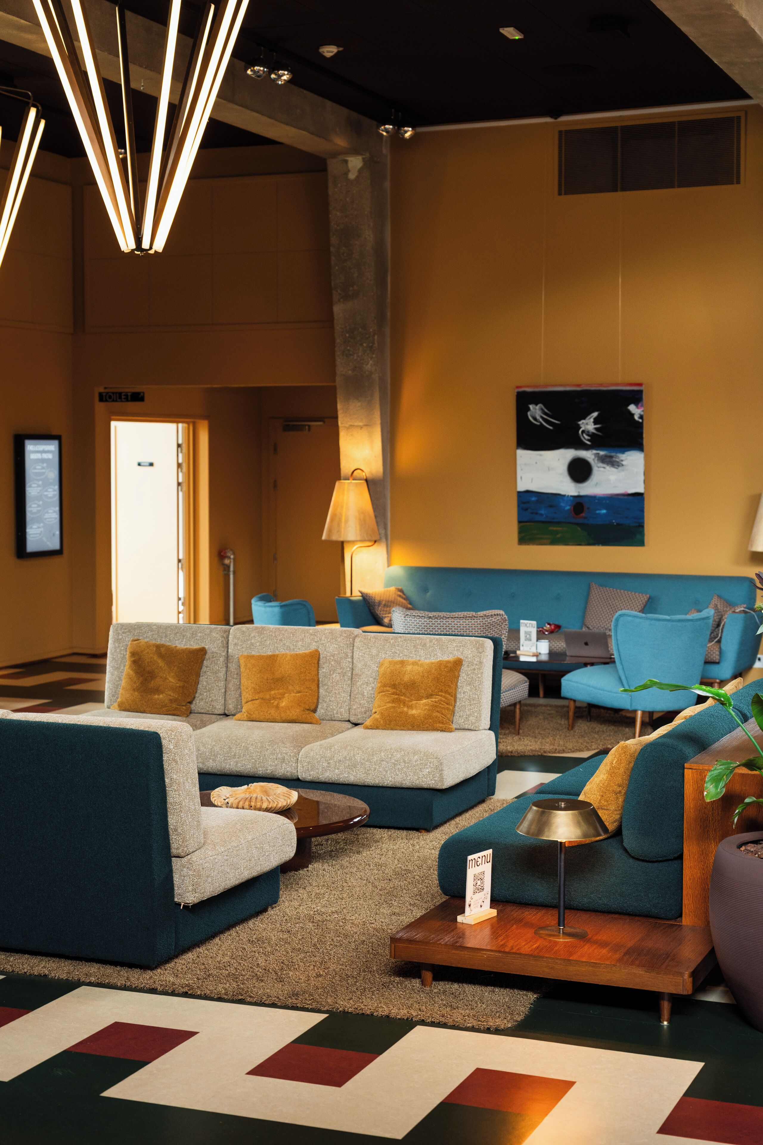 A modern lobby with a sectional sofa, a blue armchair, and a small table with a lamp.
