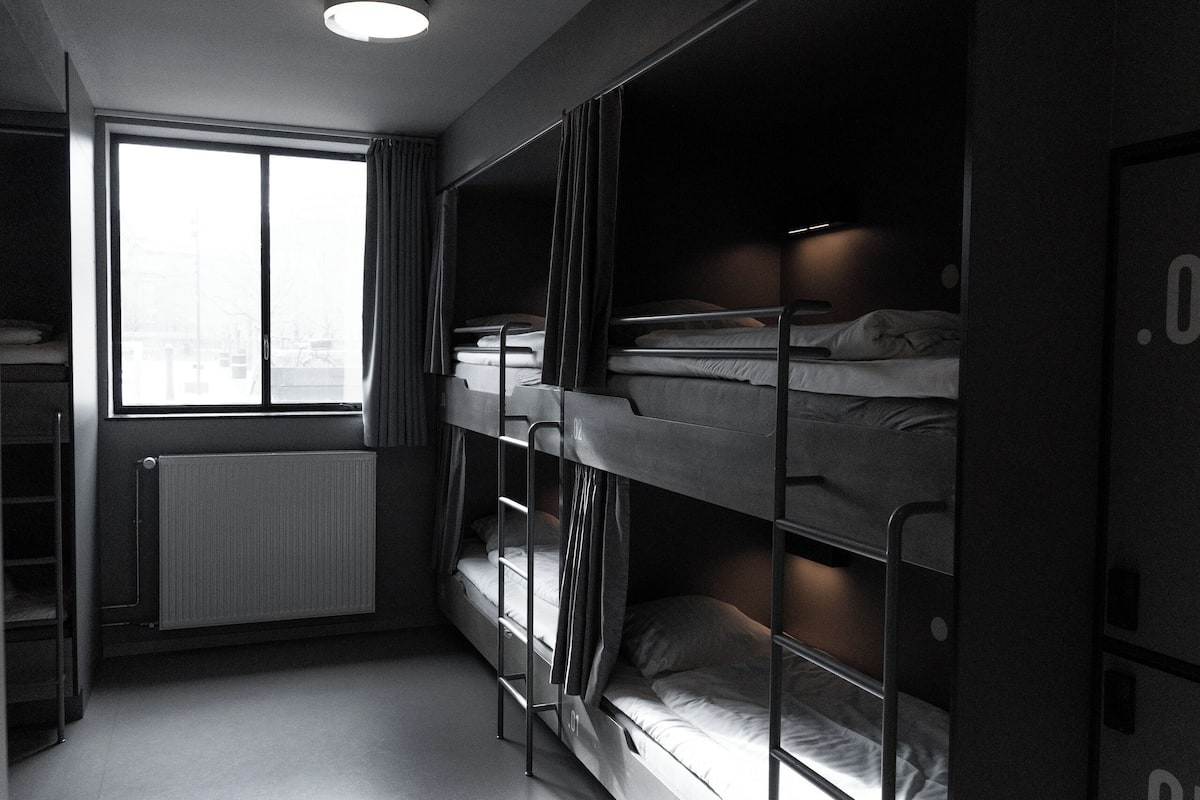 A bunk room with three bunk beds, a radiator, a window with curtains, and a ceiling light.
