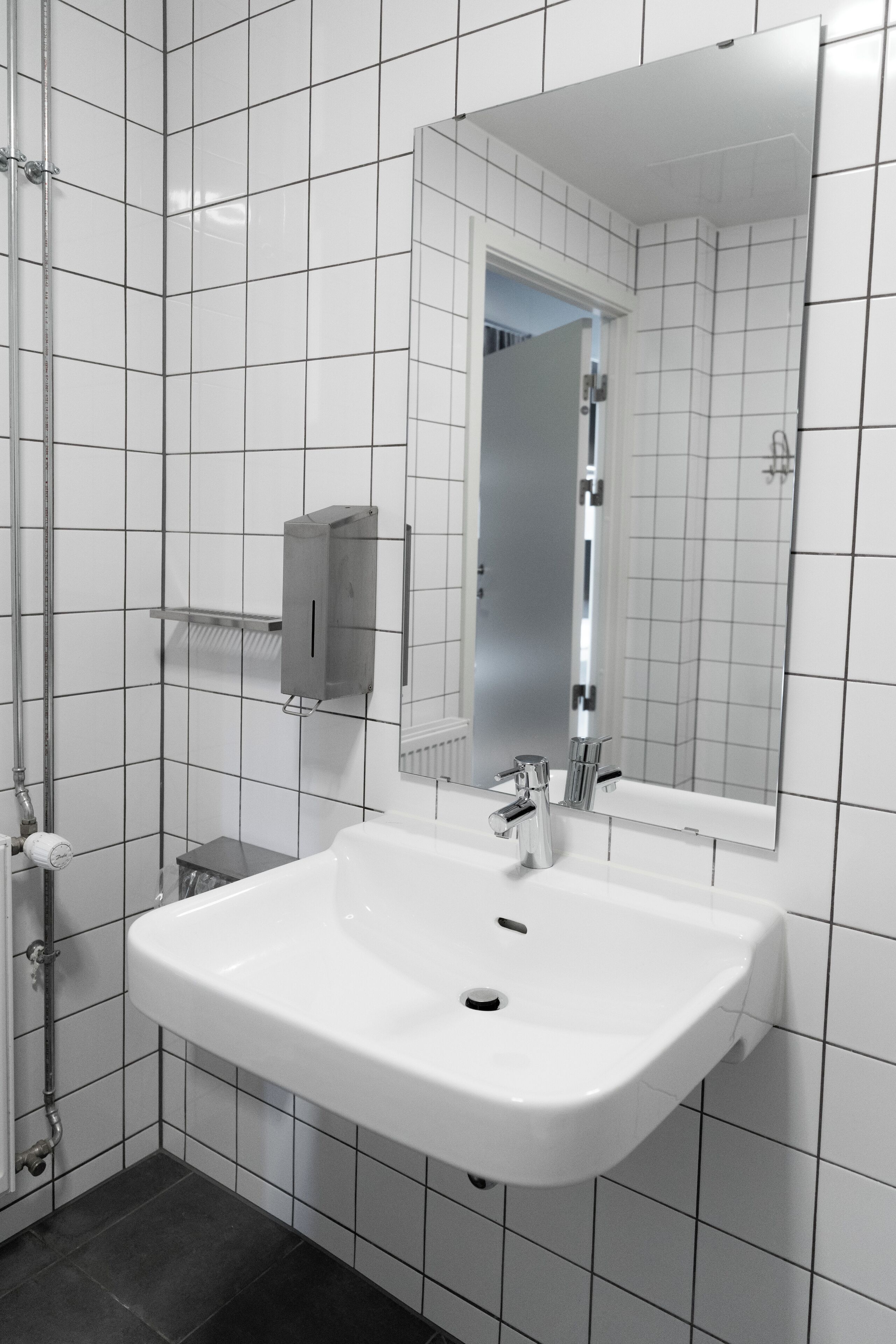 A modern bathroom with white tiled walls, a large mirror, a white sink, and a towel rack.