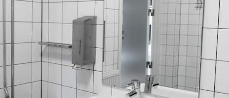 Un baño moderno con paredes de azulejos blancos, un espejo grande, un lavabo blanco y un perchero para toallas.