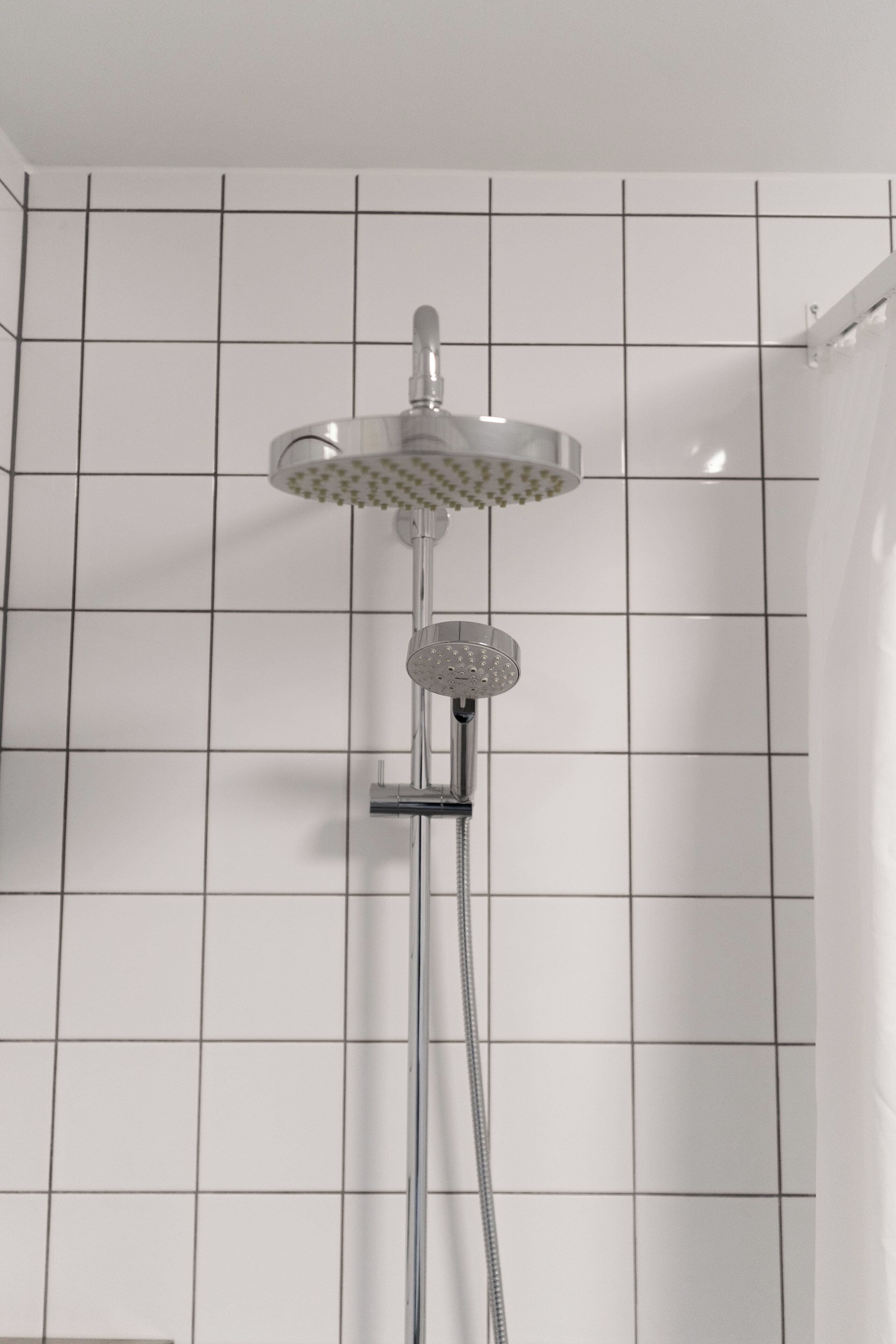 Une douche équipée d’un pommeau de douche à main et d’un pommeau de douche fixe, le tout fixé sur une robinetterie chromée.