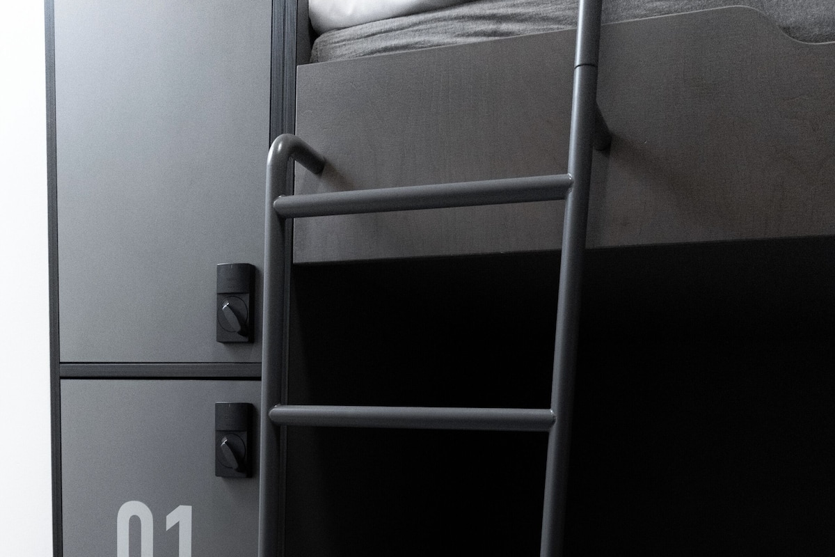 A bunk bed with a ladder, a small cabinet with a lock, and a number "01" on the cabinet.