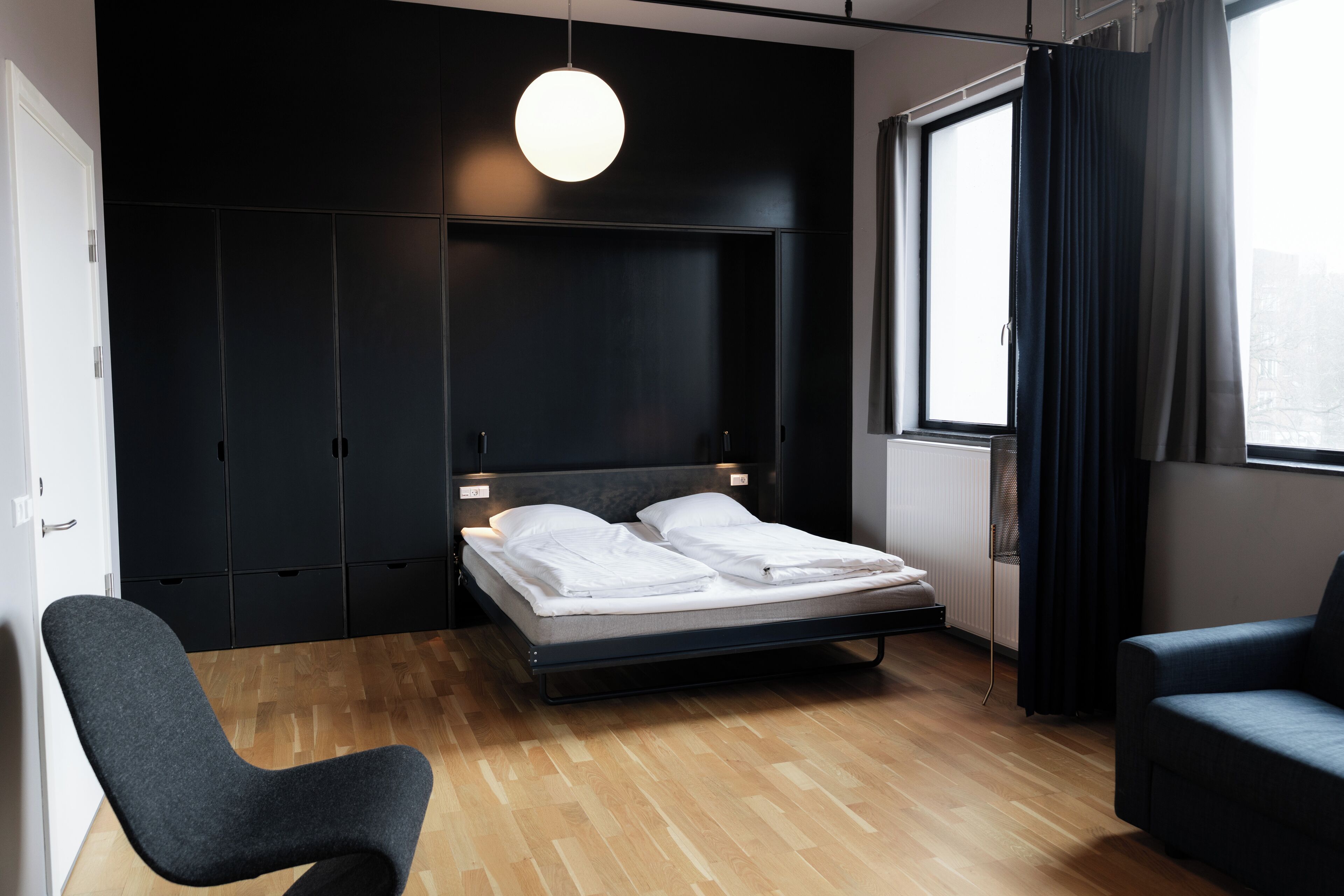 A modern bedroom with a bed, a chair, a sofa, and a large window.