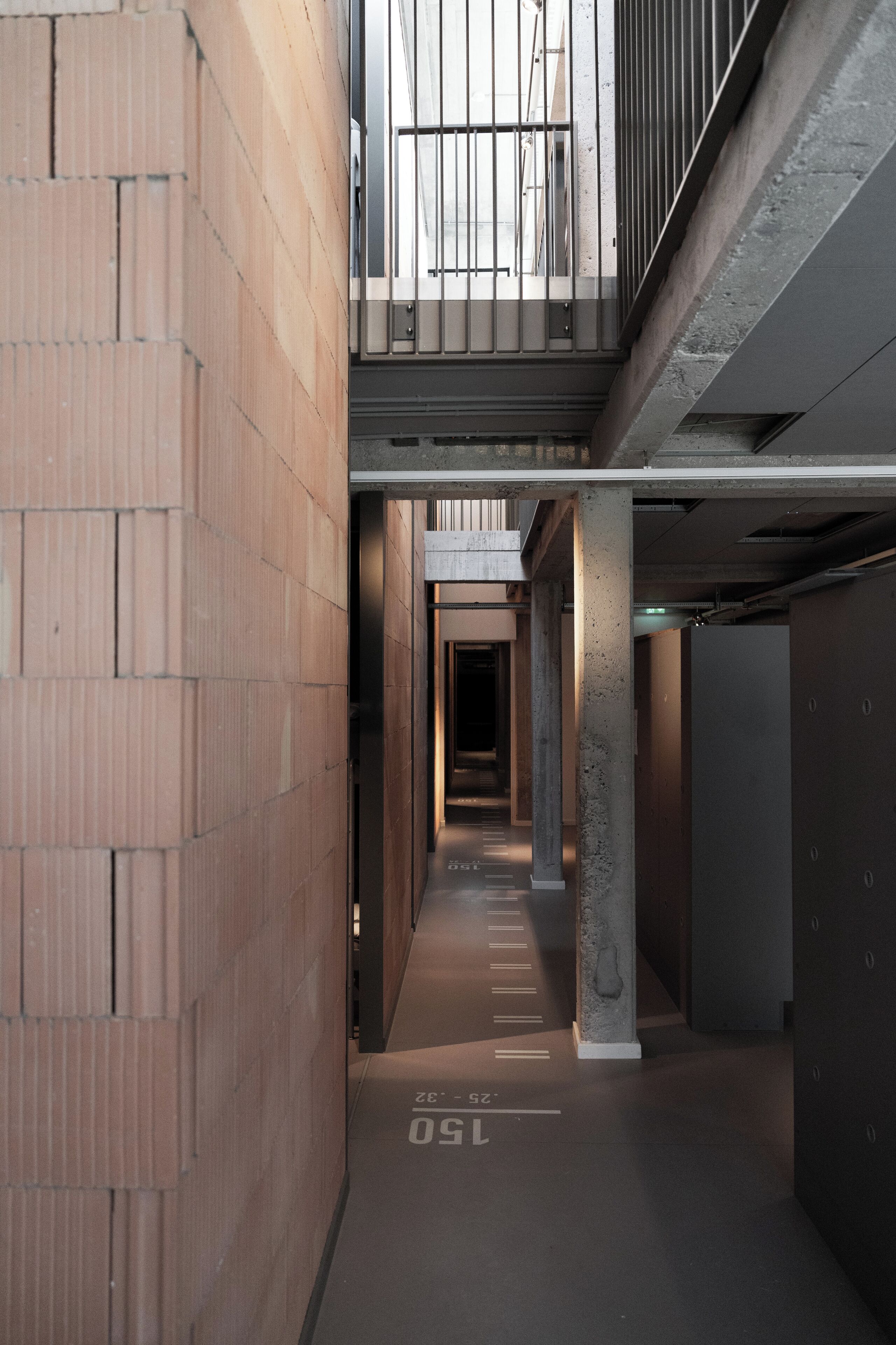 A modern building with a brick facade, concrete pillars, and a metal railing on the upper level.