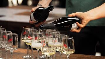 A person pouring a liquid from a bottle into several glasses on a wooden table.