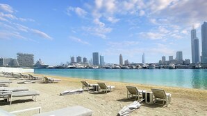 A beachside view with lounge chairs and a marina in the background. - LUX The Marina Vista Beachfront Suite 4 (Dubai)