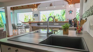 Une cuisine moderne dotée d’un évier en acier inoxydable, d’un plan de travail en bois et offrant une vue sur l’espace repas extérieur.