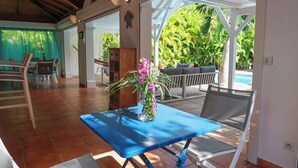 Une pièce avec une table bleue et une chaise, un vase rempli de fleurs, et une vue sur une piscine et la verdure à l’extérieur.