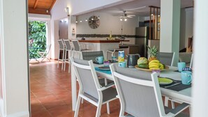 Un coin repas avec une table dressée pour quatre personnes, des chaises, une cuisine en arrière-plan et une vue sur la verdure à l’extérieur.