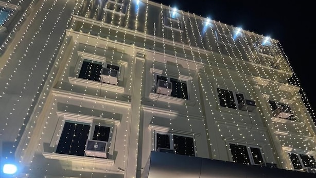 A building with multiple floors, decorated with string lights. There is a floral archway at the entrance, and several potted plants are placed outside. - Hotel Kavana (Varanasi)