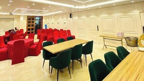 A conference room with red chairs, green chairs, and a wooden table. - Hotel Kavana (Varanasi)
