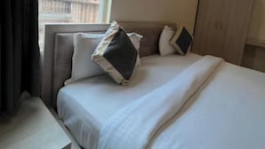 A hotel room with a bed, a nightstand, a window with a view of a temple, and a painting on the wall. - Hotel Kavana (Varanasi)