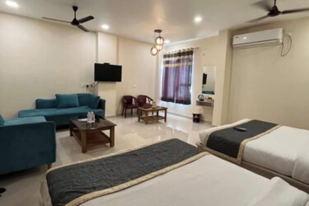 A hotel room with two beds, a sofa, a coffee table, a TV, and ceiling fans.