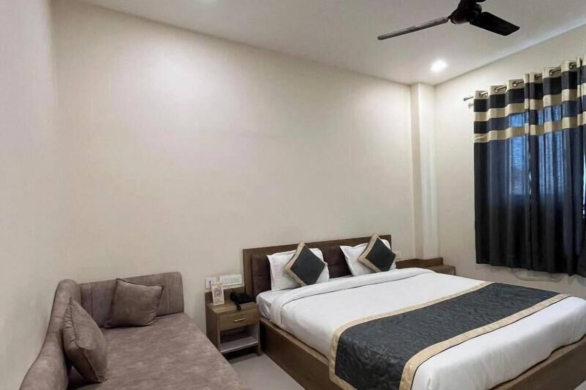 A bedroom with a bed, a sofa, a ceiling fan, and curtains.