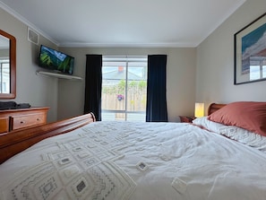 Un dormitorio con cama, televisor, cómoda y ventana con cortinas.
