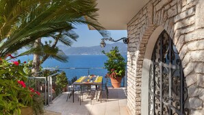 A terrace with a table set for dining, overlooking a body of water and mountains. - Villa Vista Lago With Pool (Torri del Benaco)