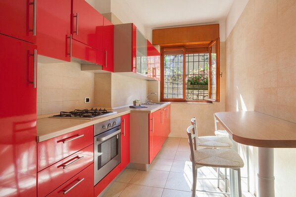 A kitchen with red cabinets, a gas stove, an oven, and a window with a view of greenery.