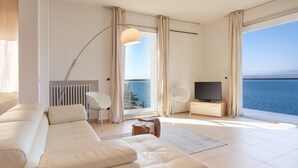 A modern living room with a sofa, TV, and large windows overlooking the sea. - Villa Vista Lago With Pool (Torri del Benaco)