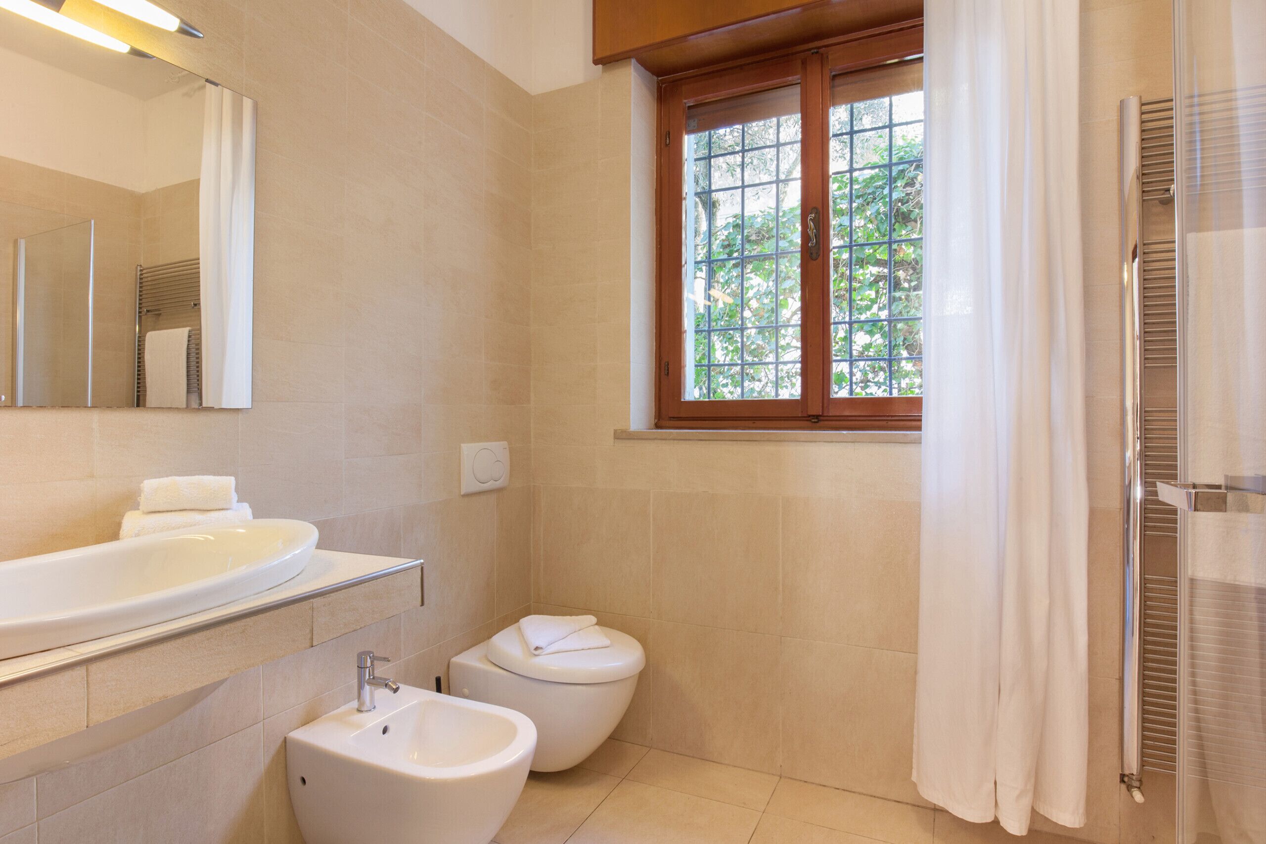 Une salle de bain équipée d’un lavabo, d’un bidet, de toilettes et d’une fenêtre avec des rideaux.
