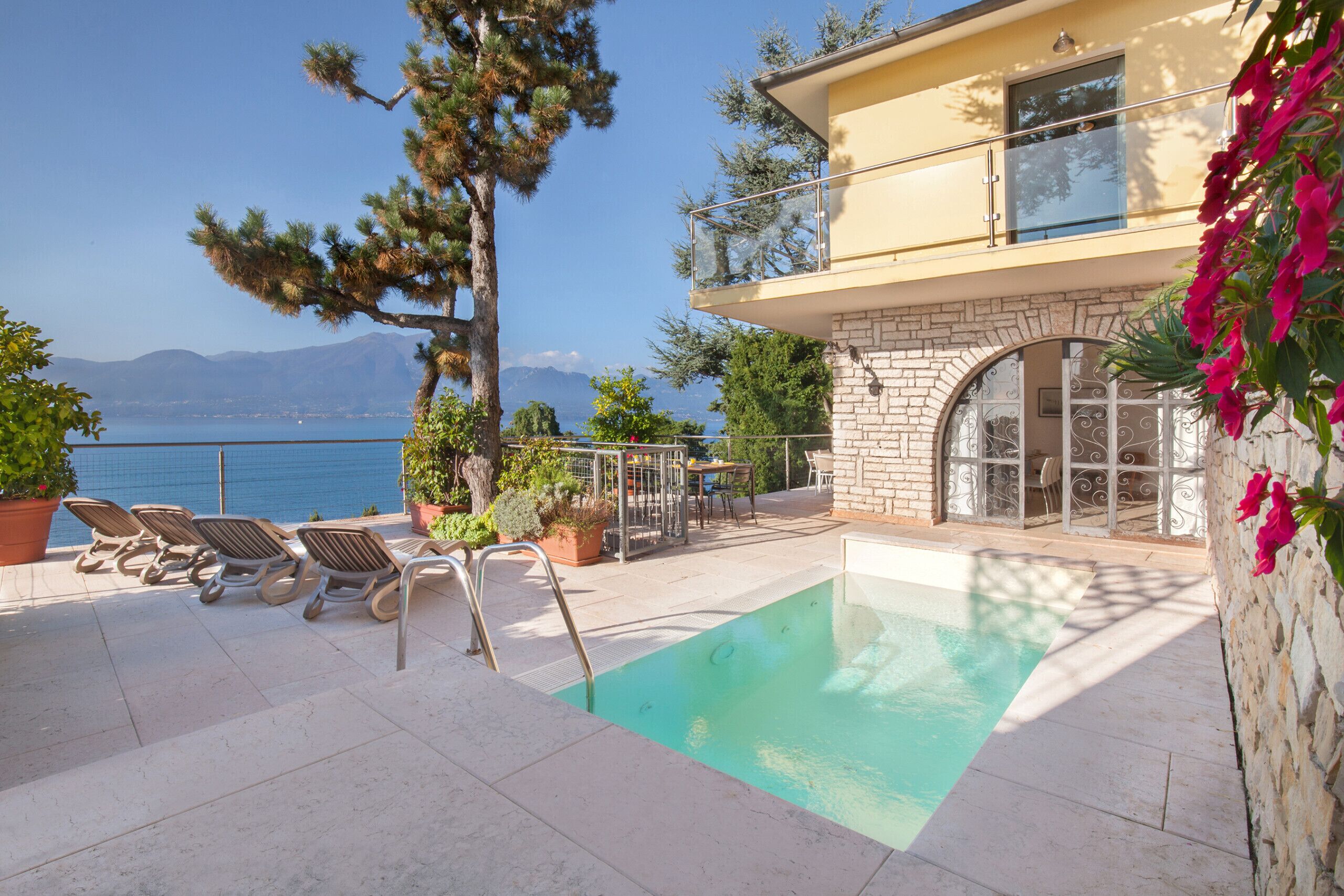 Ett poolområde med solstolar, en stenmur och utsikt över havet.